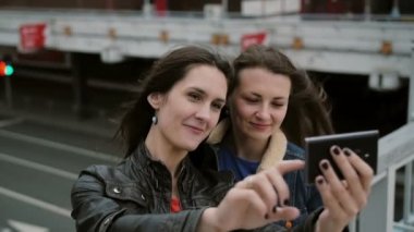 İki kız en iyi arkadaş selfie çekiyor, şehir köprüsünde duruyor, konuşuyor, gülümsüyor, gülüyor. yavaş mo.