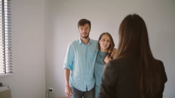 Um casal está olhando para o exterior de uma sala branca enquanto conversa com uma mulher de blazer preto. Devagar, Steadicam atirou. — Vídeo de Stock