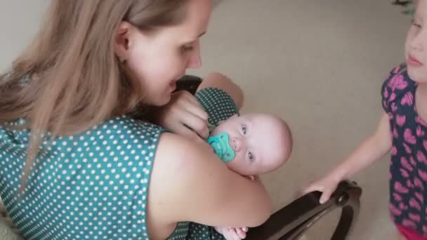 Soeur embrassant son frère nouveau-né que sa mère tient alors qu'elle est assise dans une chaise berçante . — Video