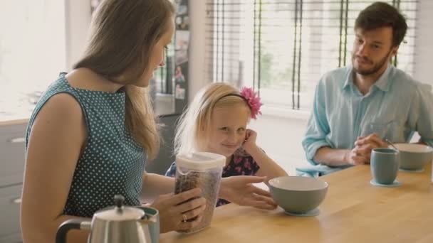 幸せな若い家族:お母さん、お父さんとその娘は台所のテーブルで朝食を食べています。スローモーション、ステディカムショット — ストック動画