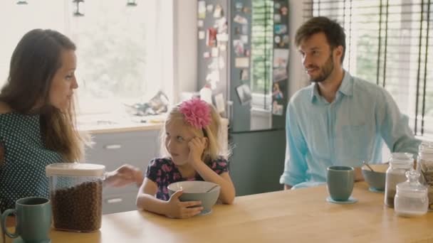 Young mother and father are smiling at their daughter who is having cereal for breakfast. Slow mo, Steadicam shot — Stock video