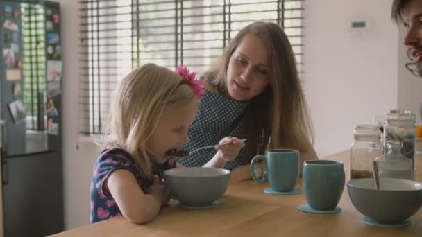 Hermosa madre joven y su linda hija rubia se ríen felizmente en la mesa de la cocina. Lento mo — Vídeo de stock