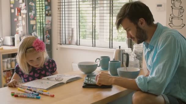 Un padre está trabajando en su iPad mientras su hija está coloreando en la mesa de la cocina. Lento mo — Vídeo de stock