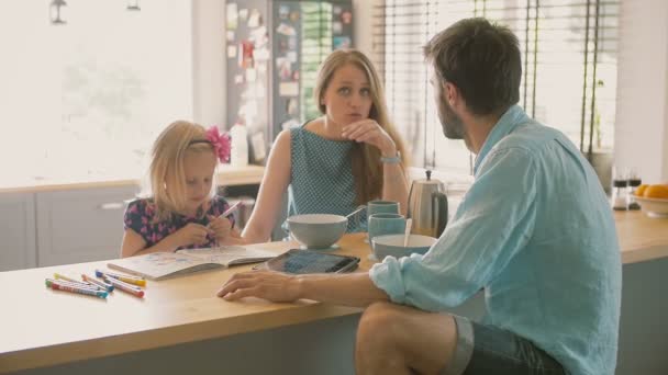 Mąż rozmawia z piękną żoną, podczas gdy ich córka jest zabarwiona na stole w kuchni. Powolne mo — Wideo stockowe