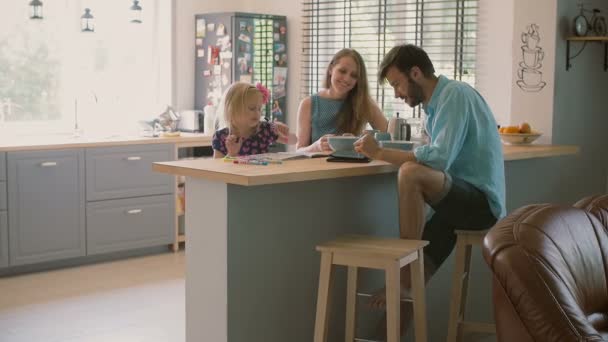 Happy wife is talking to her husband and fixing her daughters hair at the kitchen table. Slow motion — Stock Video