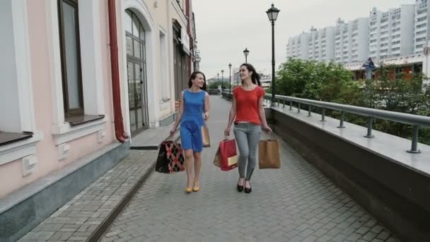 Mutlu genç kadın arkadaşlar alışveriş poşetleri ile yürürken, eğlenmeyi tartışıyorlar. yavaş mo stedicam atış — Stok video