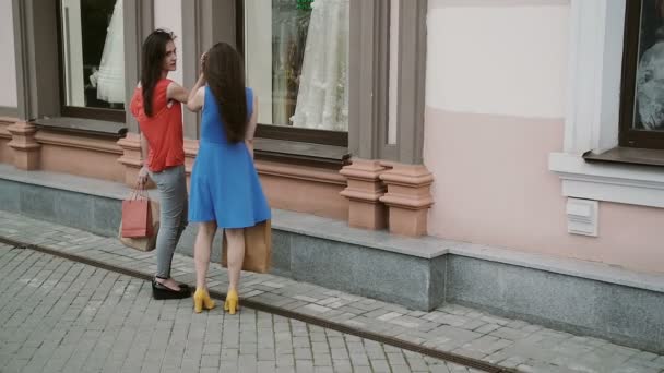 Jeunes filles amis debout près de la vitrine avec des robes de mariée et discuter. ralenti — Video