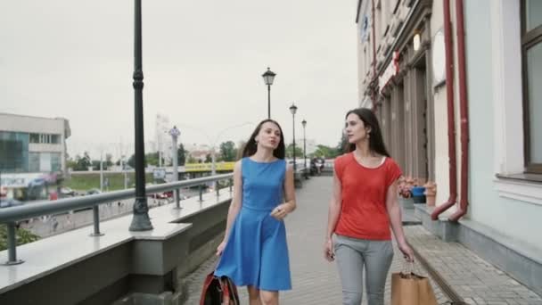 Счастливые молодые девушки-подруги ходят после покупок с сумками, обсуждают что-то медленное, стейкэмпл снимают — стоковое видео