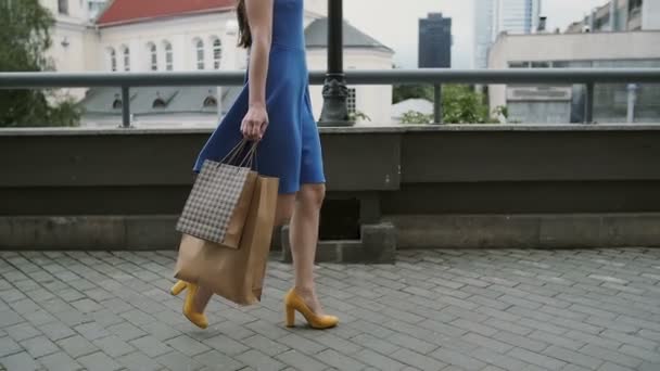 Jambes mince jeune femme, marcher dans la ville en bas de la rue avec des sacs à provisions, vue latérale, slow mo, stedicam shot — Video