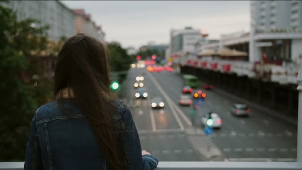 Vacker flicka stående på bron, tittar på staden, sedan vänder sig till kameran och leende. Vinden blåser håret. Slow Mo — Stockvideo