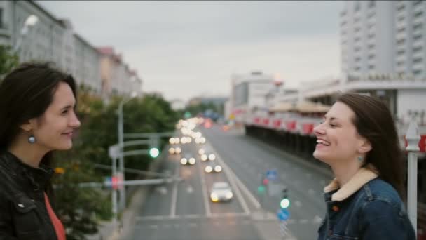 Dos hermosas chicas mejores amigas se conocieron en el puente de la ciudad, abrazándose, besándose, hablando, sonriendo, riendo. lento mo — Vídeos de Stock