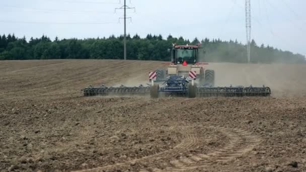 An agricultural tractor, plowing a field before sowing, moving from the camera. A forest in the background. — Stock Video