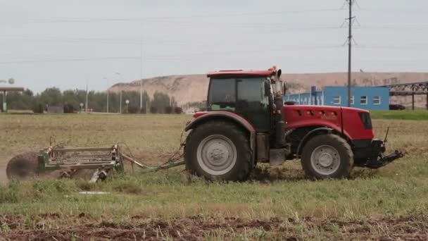 Vue latérale d'un tracteur agricole, labourant un champ pour semer. Les oiseaux volent et atterrissent sur le terrain . — Video