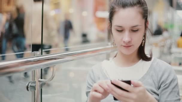 Mladá brunetka žena v šedém svetru pomocí svého smartphonu. — Stock video