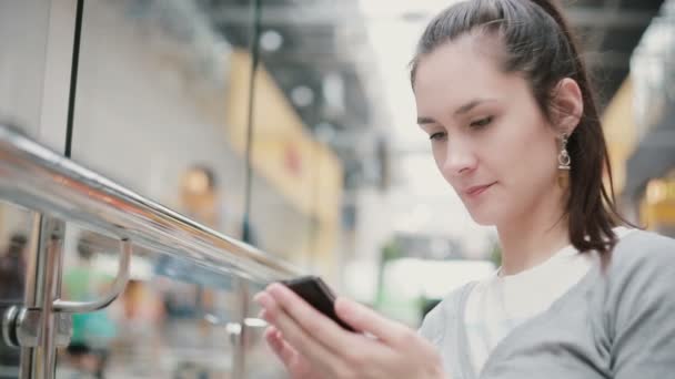 Een meisje met mooie oorbellen en een paardenstaart zit in een openbare plaats, typen op haar telefoon. — Stockvideo