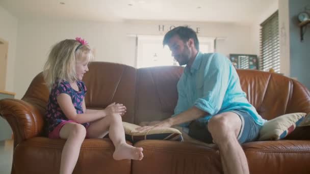 一个年轻的父亲和可爱的快乐小女儿正在玩帕特一蛋糕在客厅里的沙发上。慢动作 — 图库视频影像