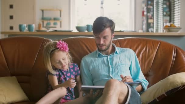 Niña rubia está eligiendo una historia que su amoroso padre leerá en el sofá. Movimiento lento — Vídeos de Stock