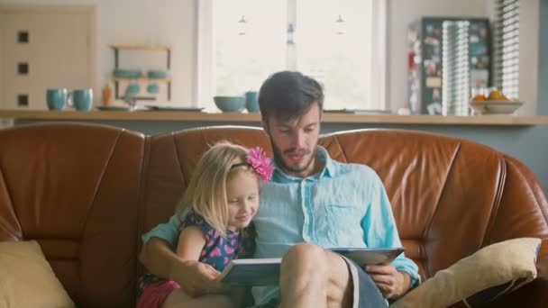 Genç bir baba ve mutlu küçük sarışın kızı deri kanepe yemek salonunda bir hikaye okuyor. Ağır çekim