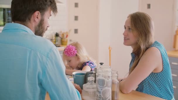 Jovens pais conversando na mesa da cozinha enquanto sua filha está colorindo. Devagar. — Vídeo de Stock