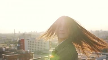 young woman standing on the roof at sunset turns the head and her hair looking at the camera. slow mo