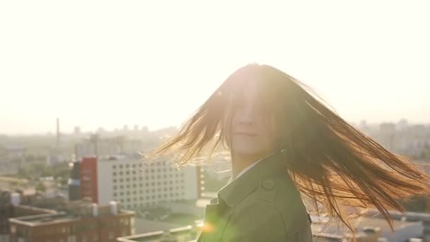 Jeune femme debout sur le toit au coucher du soleil tourne la tête et ses cheveux en regardant la caméra. ralenti — Video