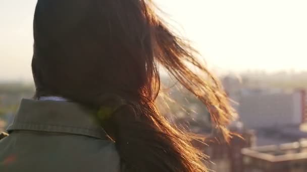 Vista trasera. El viento sopla pelo largo oscuro hermosas mujeres jóvenes. chica de pie en el techo al atardecer. Lento mo — Vídeos de Stock