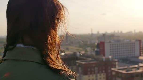 Achteraanzicht. Wind waait lang haar mooie jonge vrouwen. meisje staat op het dak bij zonsondergang. Slow mo — Stockvideo