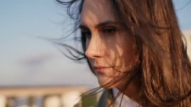 Στοχαστική νεαρή όμορφη γυναίκα στέκεται στην οροφή στο ηλιοβασίλεμα, μακριά σκούρα μαλλιά της φυσάει άνεμος. αργή κίνηση. — Αρχείο Βίντεο