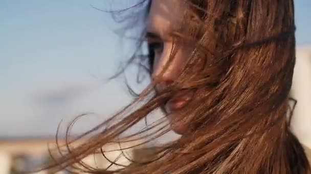 Вдумчивая молодая красивая женщина, стоящая на крыше на закате, ее длинные темные волосы дуют ветром. замедленное движение . — стоковое видео