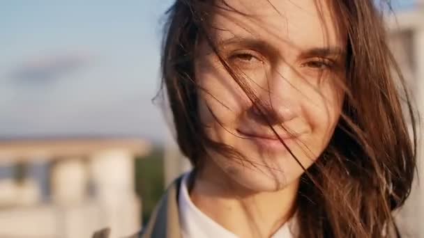 Felice donna sorridente in piedi sul tetto al tramonto, guardando la fotocamera i suoi lunghi capelli scuri che soffiano vento. rallentatore . — Video Stock