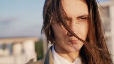 Young beautiful woman standing on the roof at the sunset, her long dark hair blowing wind. slow motion.