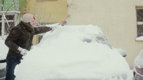 Чоловік розчищає сніг зі своєї машини на вулиці взимку, вид спереду, проміжок часу , — стокове відео