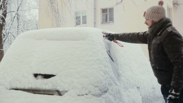 Man wist sneeuw uit zijn auto op straat in de winter, achteraanzicht, — Stockvideo