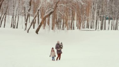 Karlı bir parkta çocuklarıyla duran genç bir anne.