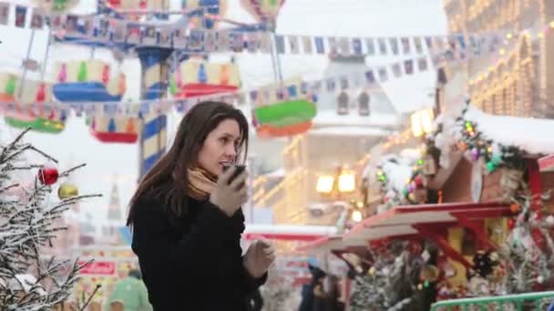 Mujer hablando por teléfono de pie en el invierno en el mercado de Navidad en la Plaza Roja en Moscú, Rusia . — Vídeos de Stock