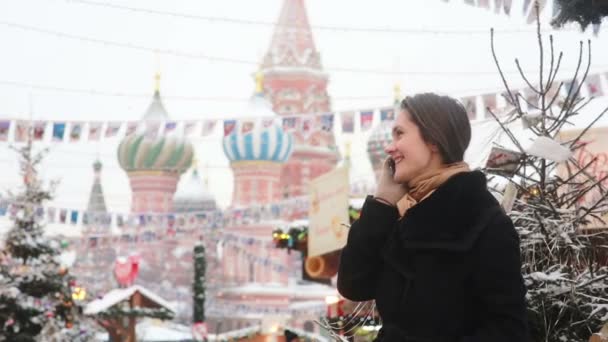 Woman talking on the phone standing in the winter on the Red Square in Moscow, in front of St. Basil Cathedral — Stok video