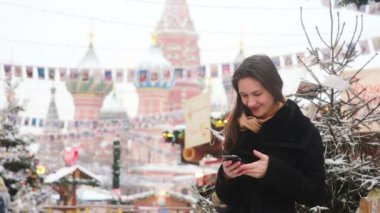 Kışın Moskova 'daki Kızıl Meydan' da St. Mary 'nin önünde akıllı telefon kullanan bir kadın. Fesleğen Katedrali