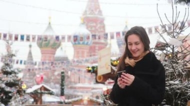 Woman talking on the phone standing in the winter on the Red Square in Moscow, in front of St. Basil Cathedral