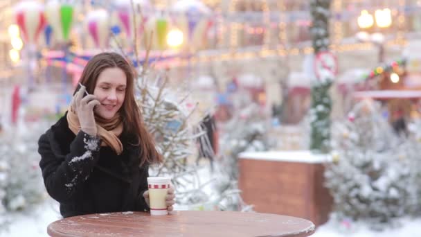 美丽的年轻女子在圣诞博览会期间打电话和喝热茶 — 图库视频影像