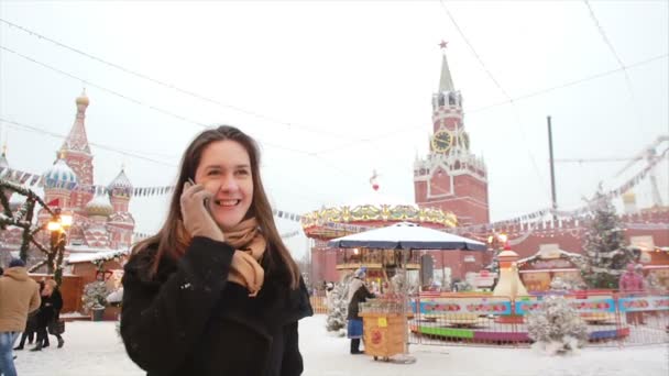 Woman talking on phone standing in the winter on the Red Square in Moscow, in front of Kremlin and St. Basils Cathedral — 图库视频影像