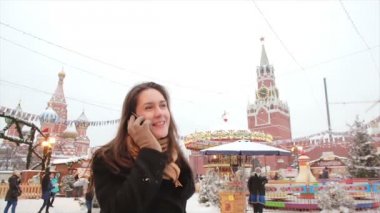 Woman talking on phone standing in the winter on the Red Square in Moscow, in front of Kremlin and St. Basils Cathedral