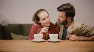 Aşık bir çift kahve içiyor, kanepede oturuyor, birbirleriyle konuşuyor ve mutlu bir şekilde gülümsüyor..