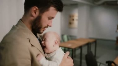 Genç bir adam kucağında bir bebek tutuyor ve konuşuyor, onu yanağından öpüyor. Loft arka plan.