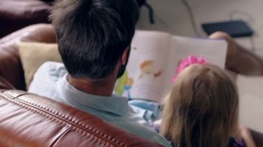 Üstten Görünüm. genç Baba ve küçük sarışın kızı deri kanepe yemek salonunda bir hikaye okuyor. 4k