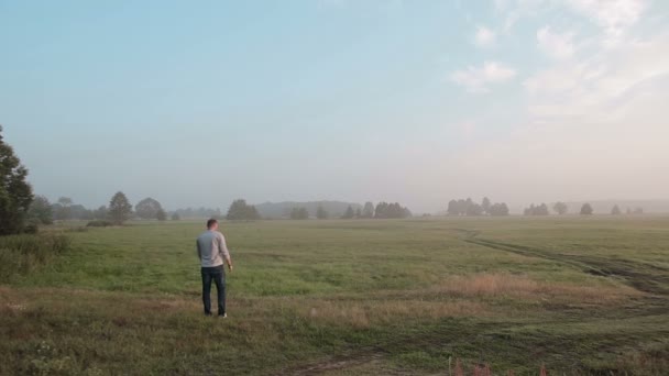 背の高い男が夏に田舎を一人で歩いている。自然は美しく、彼はゆっくりと静かに歩いている. — ストック動画