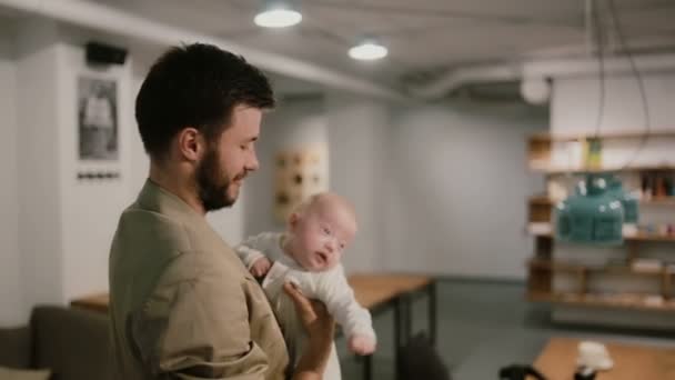 Um jovem está segurando um bebê em seus braços e falando. Fundo de Loft — Vídeo de Stock