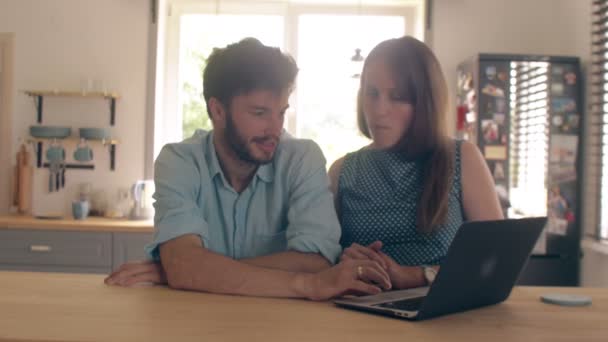 Young good-looking couple is talking at the kitchen table looking at the laptop. 4k — Stock Video