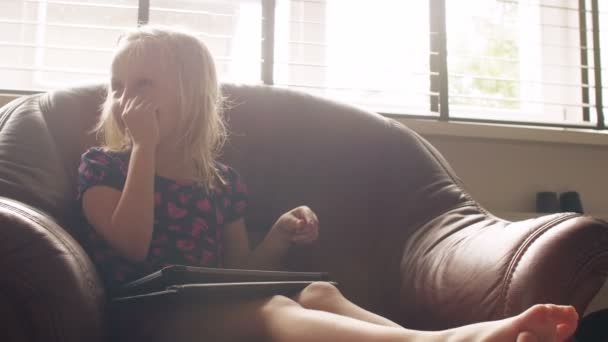Uma menina loira bonito vestindo tudo rosa issitting em uma cadeira e jogar um jogo em tablet. 4k — Vídeo de Stock