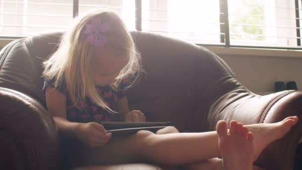 Uma menina loira bonito vestindo tudo rosa issitting em uma cadeira e usando tablet. 4k — Vídeo de Stock