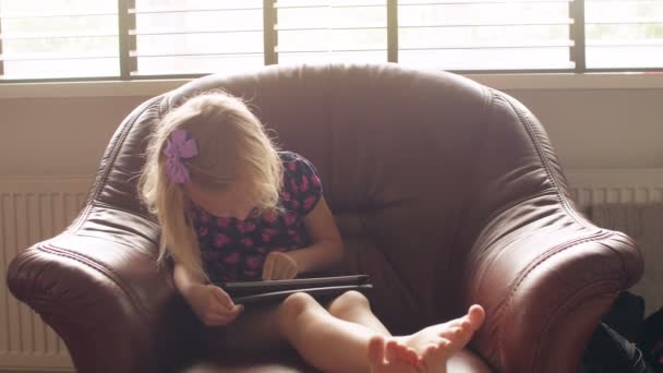 A cute blond little girl wearing all pink issitting on a chairand playing a game on tablet. 4k — Stock Video